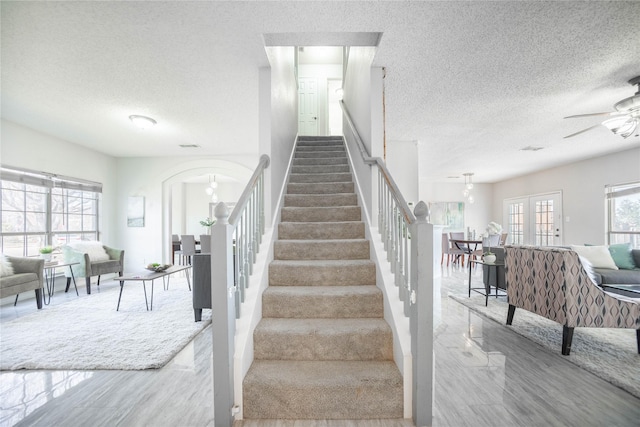 stairs featuring ceiling fan with notable chandelier and a textured ceiling