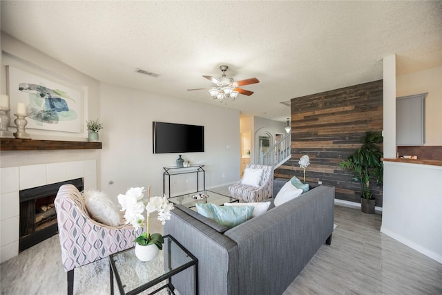 living room featuring a tile fireplace, a textured ceiling, ceiling fan, and wooden walls