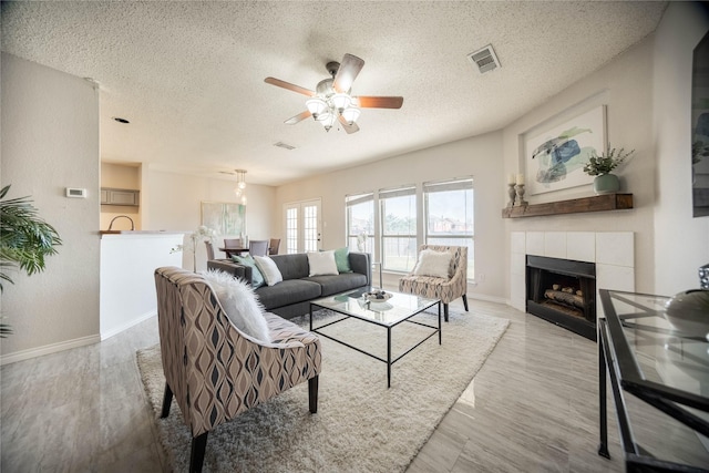 living room featuring a tile fireplace, a textured ceiling, ceiling fan, and light wood-type flooring