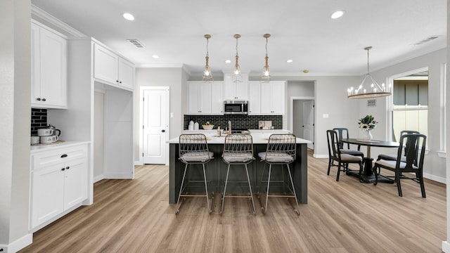 kitchen with hanging light fixtures, white cabinets, ornamental molding, and a center island with sink