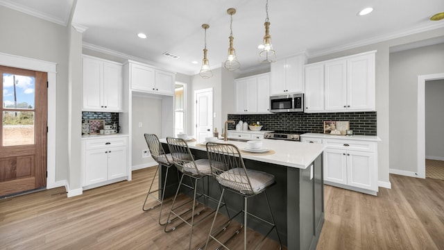 kitchen featuring decorative light fixtures, a center island with sink, white cabinetry, appliances with stainless steel finishes, and a kitchen breakfast bar