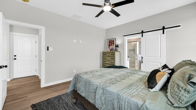 bedroom with ceiling fan, ensuite bathroom, a barn door, and hardwood / wood-style flooring