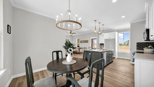 dining area with sink, ceiling fan with notable chandelier, ornamental molding, and light hardwood / wood-style flooring