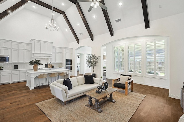 living room featuring dark wood-type flooring, ceiling fan with notable chandelier, high vaulted ceiling, and beamed ceiling