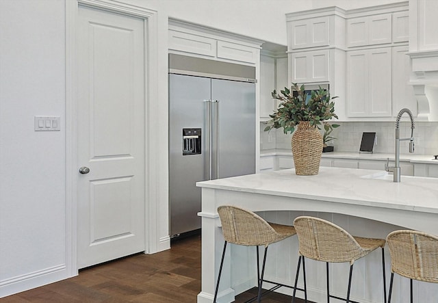 kitchen with stainless steel built in refrigerator, a kitchen bar, light stone counters, dark hardwood / wood-style floors, and white cabinets