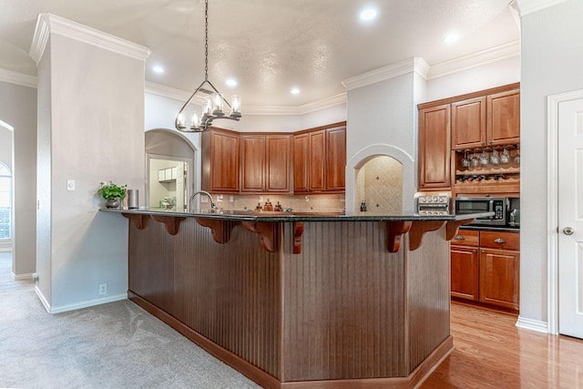 kitchen with arched walkways, backsplash, brown cabinets, stainless steel microwave, and a kitchen bar