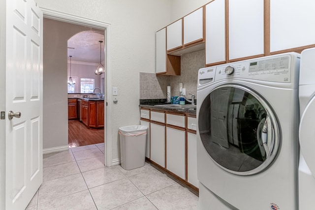 laundry area with cabinet space, light tile patterned floors, a sink, and washing machine and clothes dryer