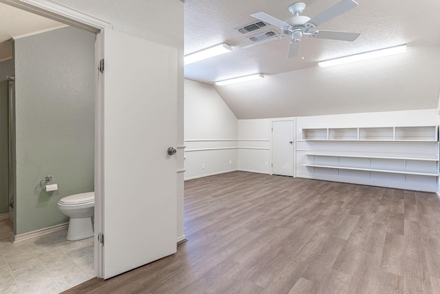 additional living space with a textured ceiling, ceiling fan, wood finished floors, visible vents, and vaulted ceiling