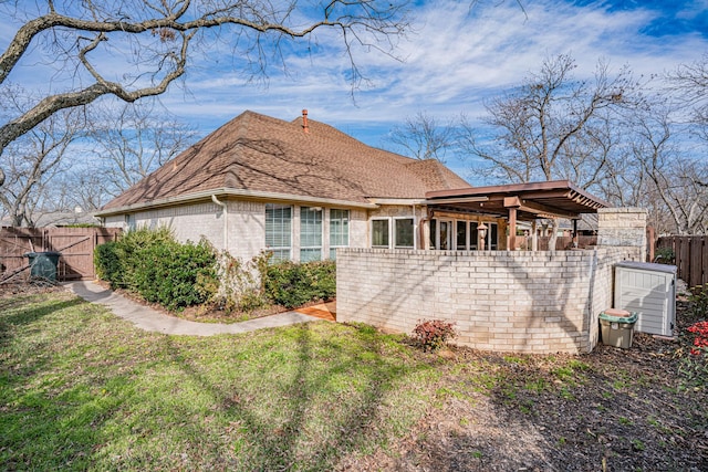 view of side of home featuring a yard, brick siding, a shingled roof, and fence