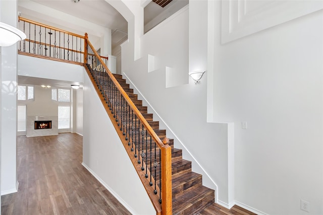 staircase featuring hardwood / wood-style floors, a towering ceiling, and a fireplace