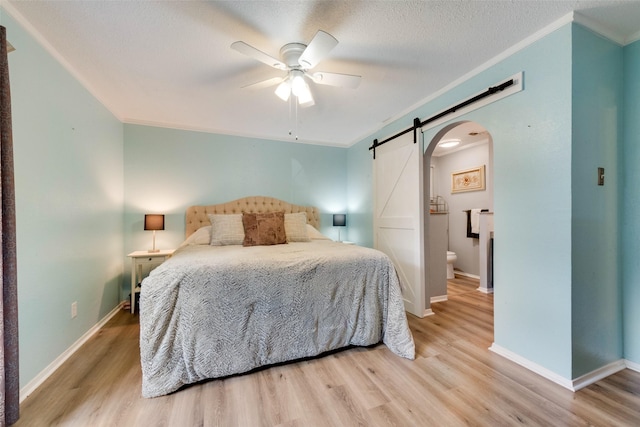 bedroom with ornamental molding, ceiling fan, light hardwood / wood-style floors, and a barn door