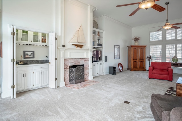 carpeted living room featuring sink, crown molding, ceiling fan, a towering ceiling, and a fireplace