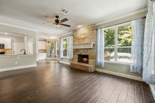 unfurnished living room with ceiling fan with notable chandelier, a wealth of natural light, ornamental molding, and a fireplace