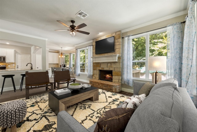 living room with ceiling fan with notable chandelier, plenty of natural light, dark hardwood / wood-style flooring, and a stone fireplace