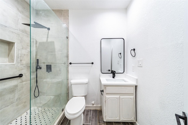 bathroom with toilet, a tile shower, and vanity