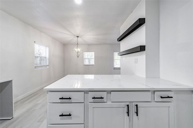 kitchen featuring white cabinetry, light stone counters, kitchen peninsula, pendant lighting, and a notable chandelier