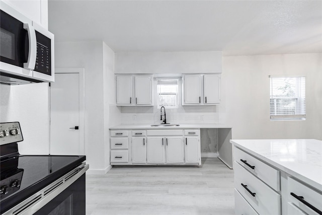 kitchen with electric stove, light wood-type flooring, backsplash, white cabinetry, and sink