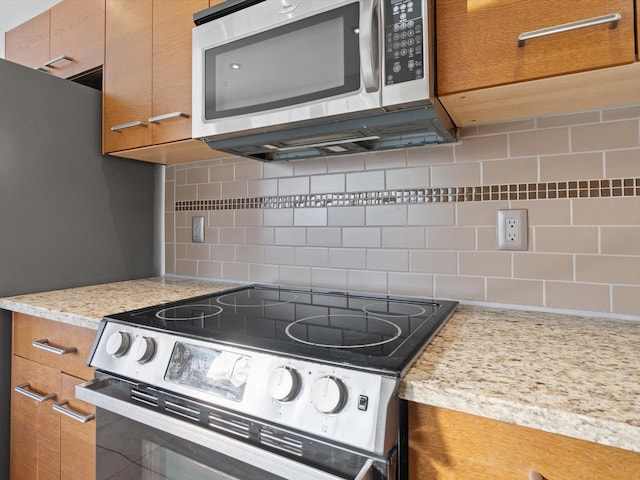 kitchen featuring stainless steel appliances, backsplash, and light stone countertops