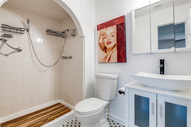 bathroom with tile patterned flooring, a tile shower, vanity, and toilet