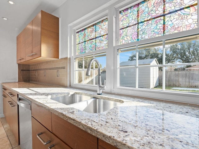 kitchen featuring light stone countertops, dishwasher, light tile patterned floors, backsplash, and sink