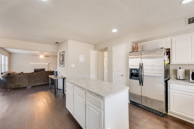 kitchen featuring white cabinetry, ceiling fan, a brick fireplace, stainless steel fridge with ice dispenser, and a kitchen island