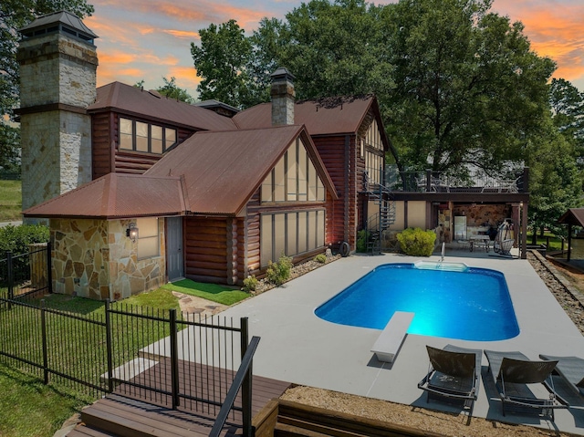 pool at dusk with a patio, a diving board, and a yard