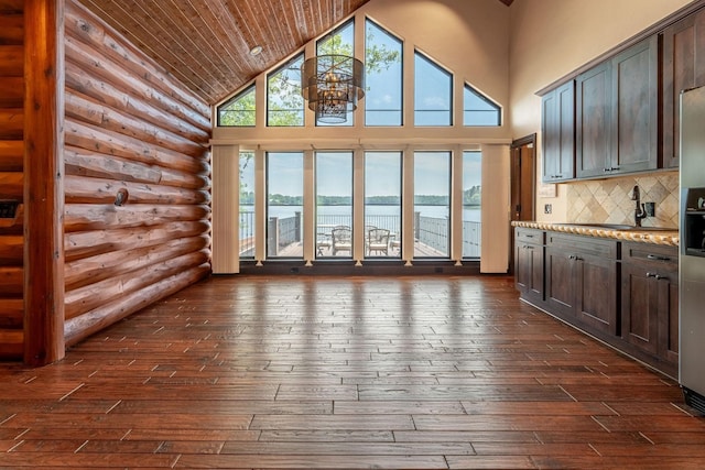 unfurnished living room with rustic walls, dark hardwood / wood-style floors, high vaulted ceiling, wooden ceiling, and a water view