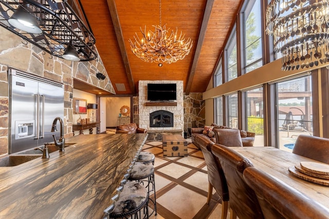 living room featuring sink, an inviting chandelier, beamed ceiling, wood ceiling, and a stone fireplace