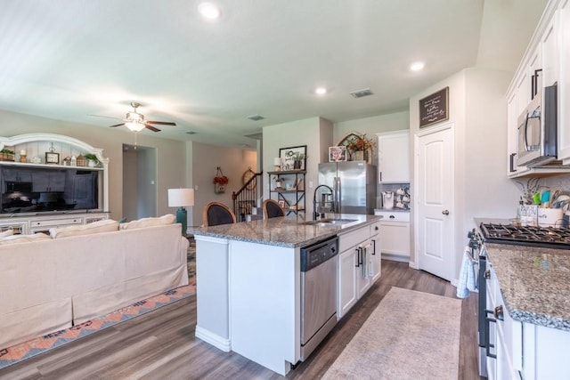 kitchen featuring a kitchen island with sink, appliances with stainless steel finishes, dark stone countertops, and white cabinetry