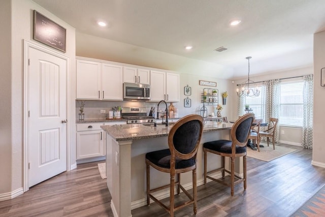 kitchen featuring white cabinetry, dark stone countertops, stainless steel appliances, and a center island with sink