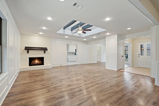 unfurnished living room featuring a skylight, a fireplace, ceiling fan, and light hardwood / wood-style floors