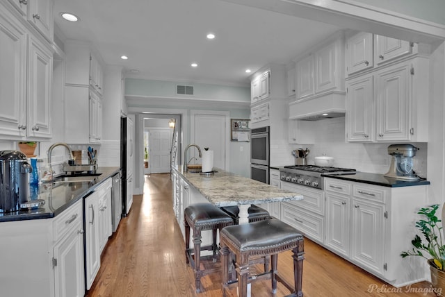 kitchen featuring sink, stainless steel appliances, white cabinetry, and a center island with sink