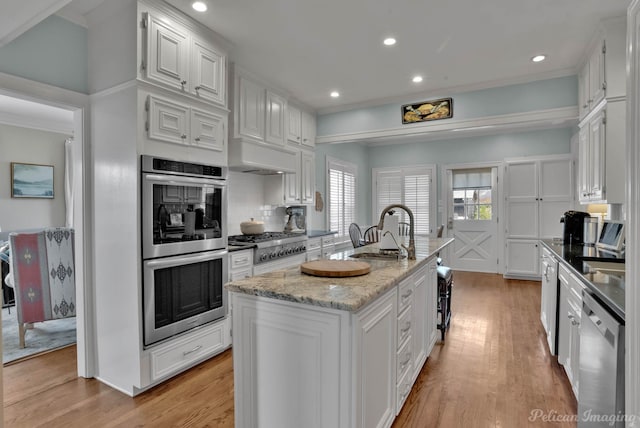 kitchen featuring stainless steel appliances, decorative backsplash, white cabinetry, and a kitchen island with sink