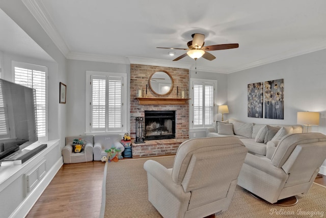 living room featuring light hardwood / wood-style floors, ceiling fan, a brick fireplace, and crown molding