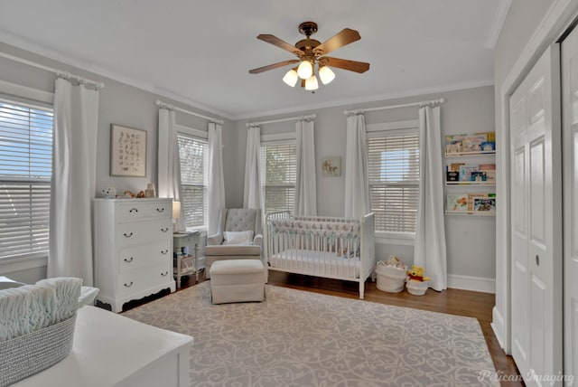 bedroom with crown molding, ceiling fan, a crib, and hardwood / wood-style floors