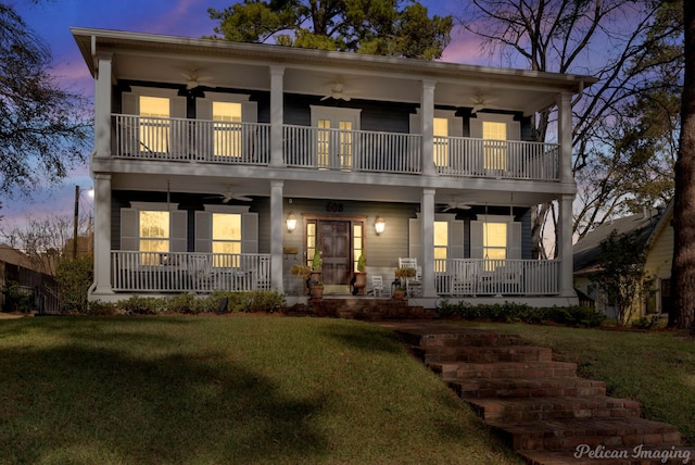 view of front of property with covered porch, a balcony, ceiling fan, and a yard