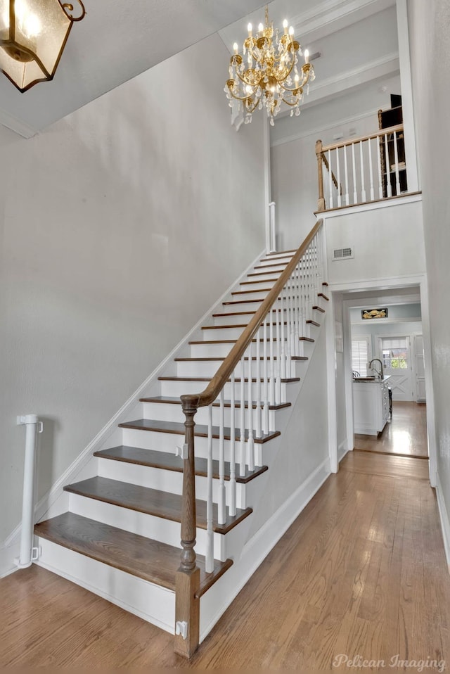 stairway with a high ceiling, hardwood / wood-style flooring, and a notable chandelier