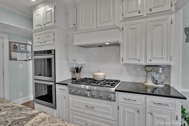 kitchen featuring custom range hood, crown molding, backsplash, white cabinets, and appliances with stainless steel finishes