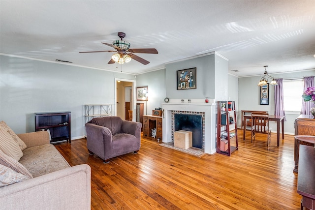 living room with hardwood / wood-style flooring, crown molding, a brick fireplace, and ceiling fan with notable chandelier