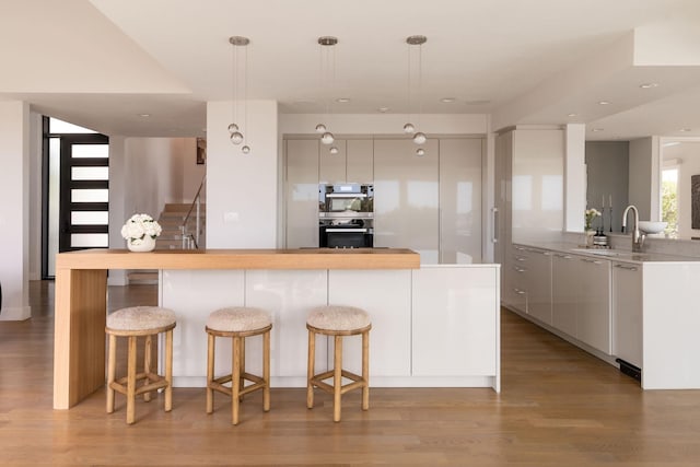 kitchen with sink, hanging light fixtures, white cabinetry, and light hardwood / wood-style floors