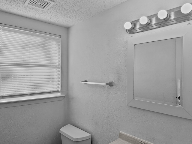 bathroom with toilet, a textured ceiling, and a healthy amount of sunlight