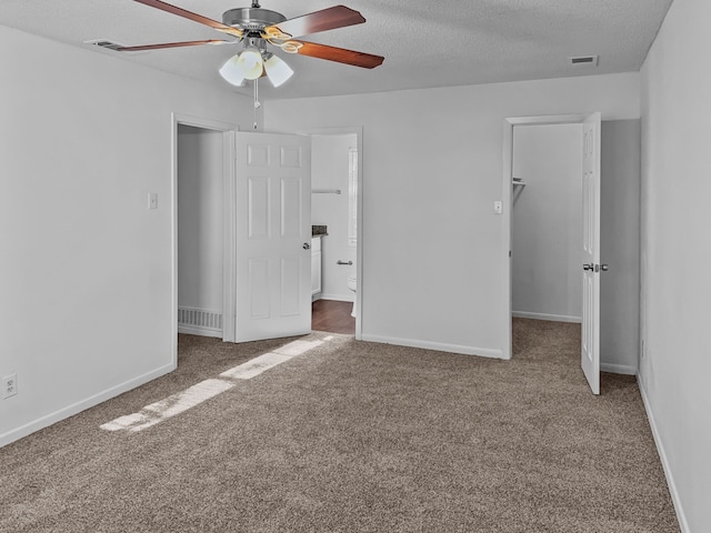 unfurnished bedroom featuring a textured ceiling, a closet, carpet, a walk in closet, and ceiling fan