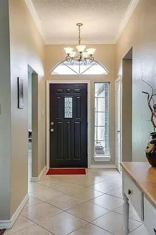 tiled entrance foyer with a textured ceiling, ornamental molding, and a notable chandelier