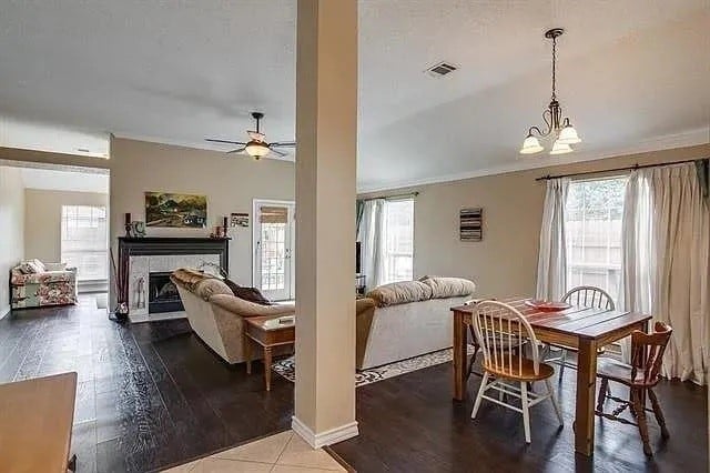 dining room with a wealth of natural light, ceiling fan with notable chandelier, hardwood / wood-style floors, and a tile fireplace