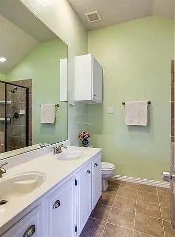 bathroom featuring toilet, vaulted ceiling, a shower with shower door, and vanity