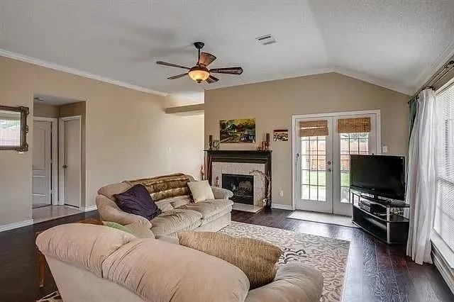 living room featuring ceiling fan, lofted ceiling, a tile fireplace, ornamental molding, and dark hardwood / wood-style flooring