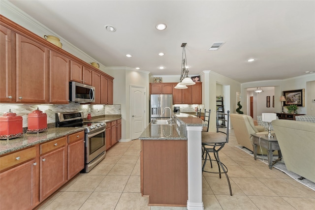 kitchen featuring hanging light fixtures, stainless steel appliances, light tile patterned floors, a kitchen bar, and a kitchen island with sink