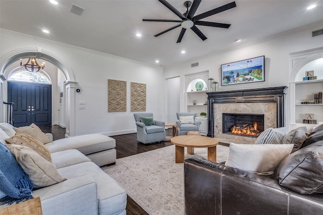 living room with dark hardwood / wood-style floors, ceiling fan with notable chandelier, a high end fireplace, built in features, and ornamental molding