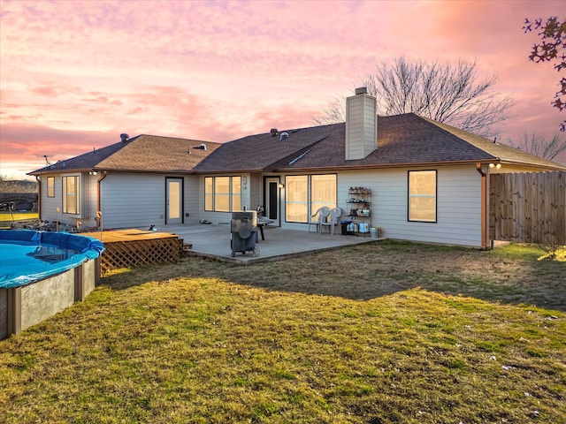 back house at dusk featuring a swimming pool side deck, a patio area, and a lawn