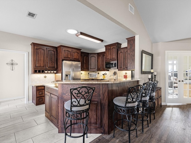 kitchen with french doors, a breakfast bar area, dark brown cabinets, stainless steel appliances, and backsplash